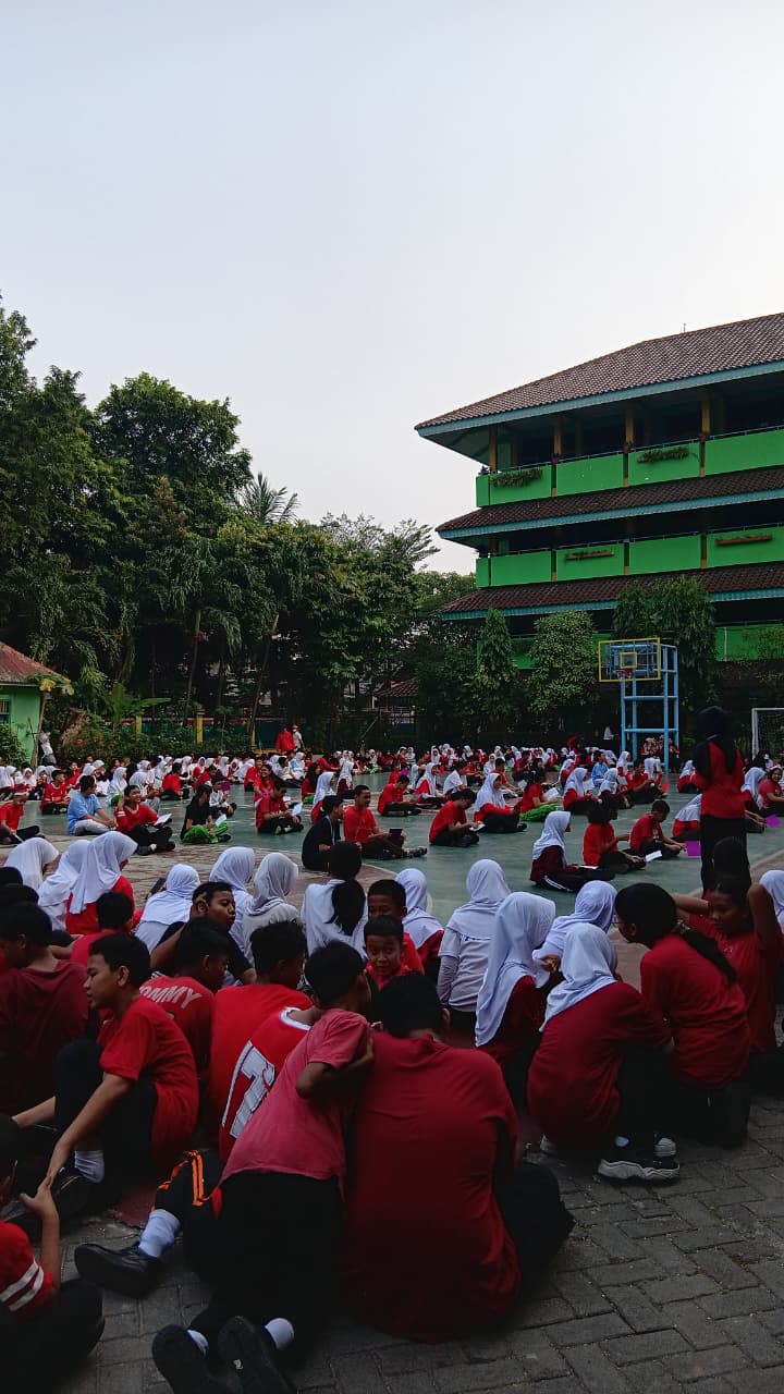 Murid berkumpul di lapangan sekolah mengenakan pakaian olahraga merah dan putih.